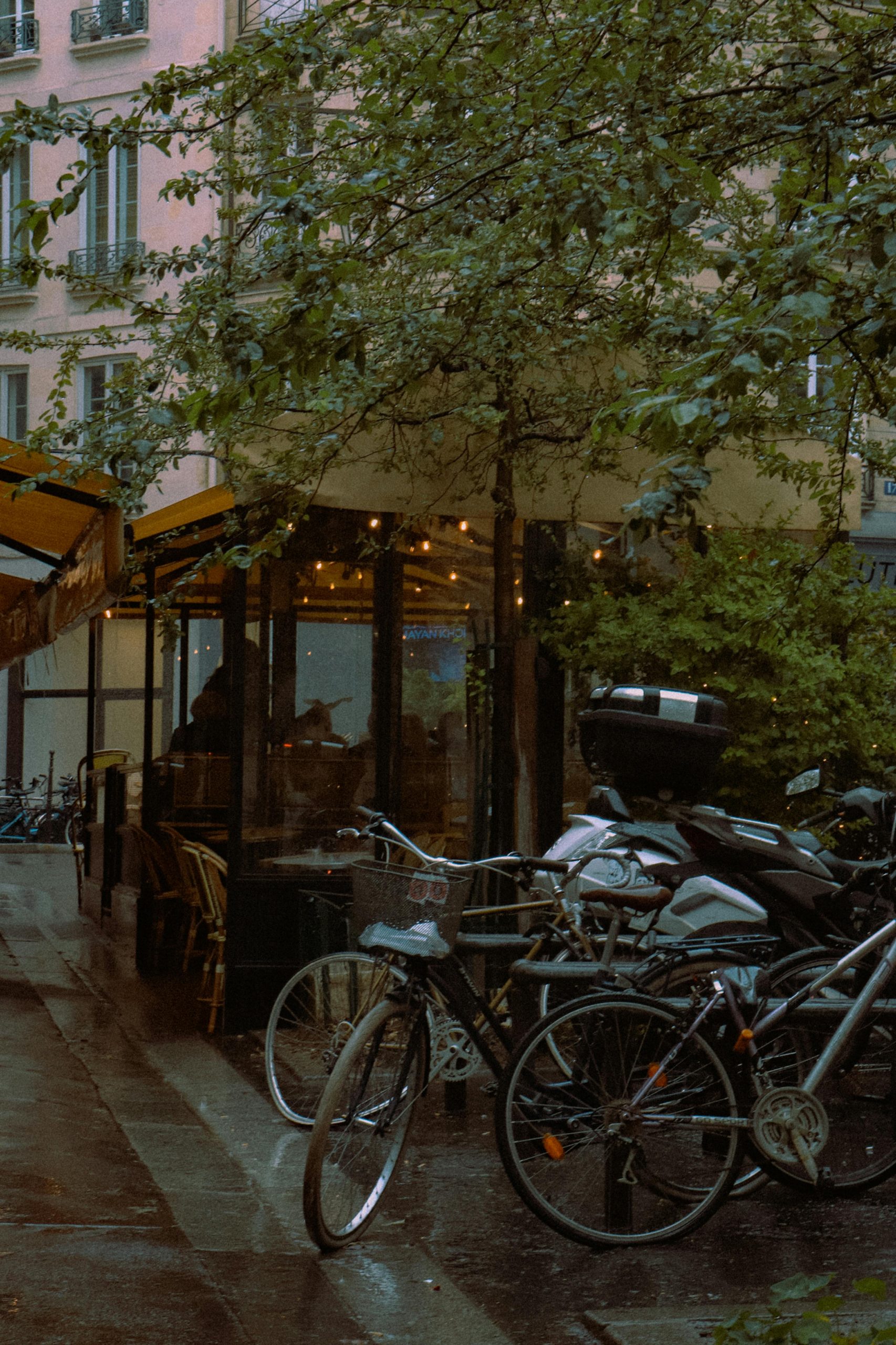 Scenic Paris street view featuring bicycles parked by a quaint café under rainy weather.